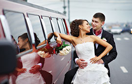 bride and groom posing outside of red hummer limousine